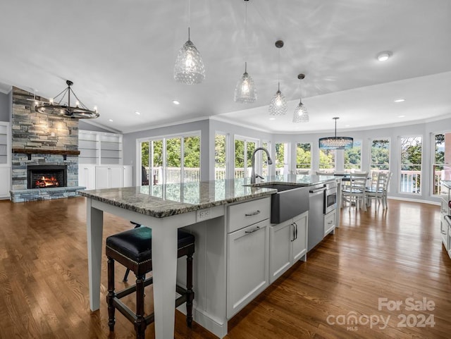 kitchen with pendant lighting, a center island with sink, sink, light stone countertops, and white cabinets