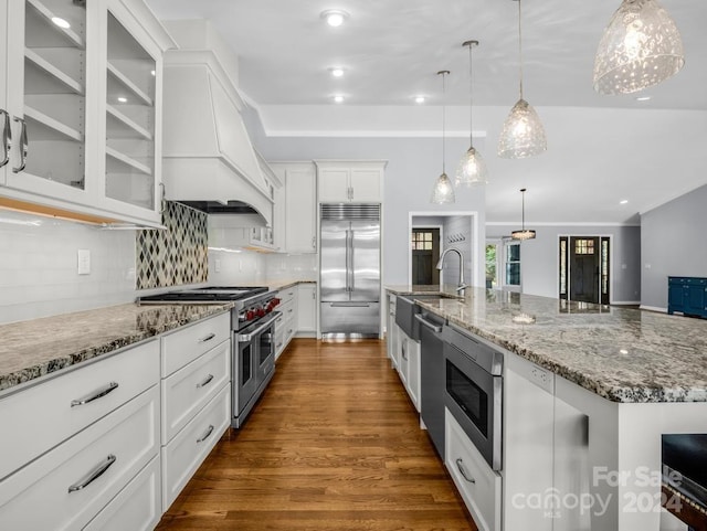 kitchen featuring pendant lighting, white cabinets, built in appliances, premium range hood, and a large island