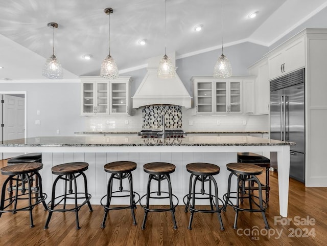 kitchen featuring stainless steel built in refrigerator, hanging light fixtures, vaulted ceiling, white cabinets, and a breakfast bar