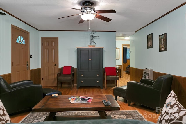 living room with light wood-type flooring, ceiling fan, ornamental molding, and wooden walls