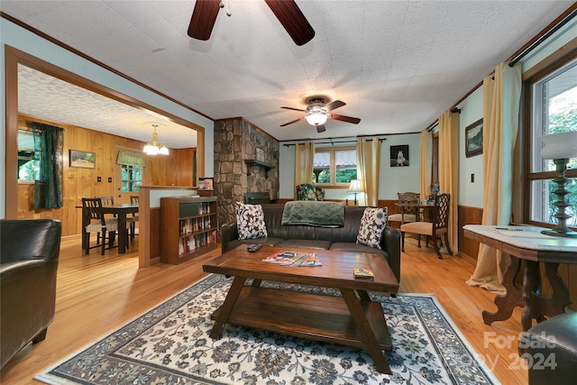 living room featuring ceiling fan with notable chandelier, crown molding, light hardwood / wood-style floors, and wooden walls