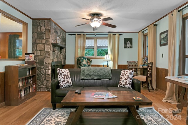 living room featuring a stone fireplace, wooden walls, light hardwood / wood-style floors, ornamental molding, and ceiling fan