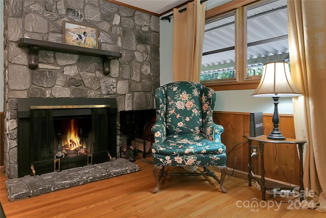 living area featuring wooden walls, crown molding, wood-type flooring, and a stone fireplace