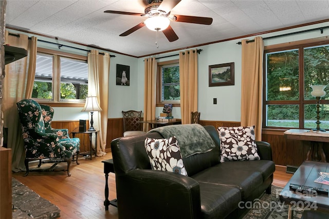 living room featuring ceiling fan, wood walls, ornamental molding, and hardwood / wood-style flooring