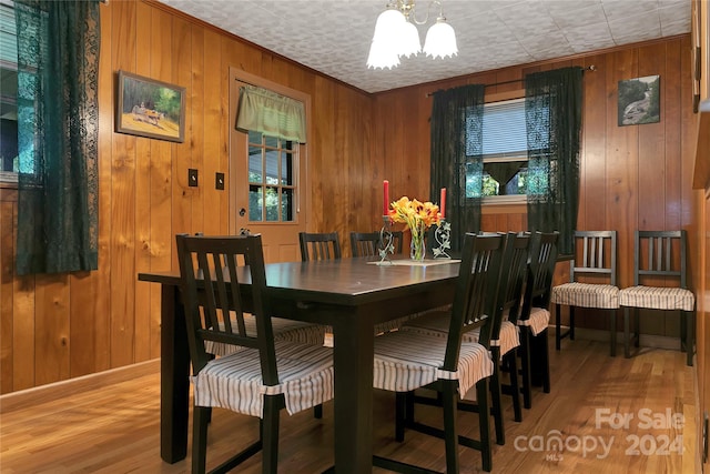 dining space featuring light wood-type flooring, wood walls, and a chandelier