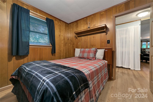 bedroom with crown molding, light hardwood / wood-style floors, and wooden walls