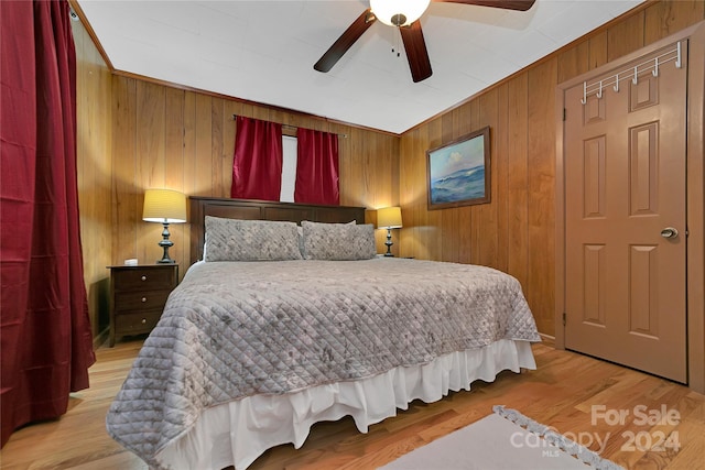 bedroom featuring ceiling fan, light hardwood / wood-style floors, and wooden walls