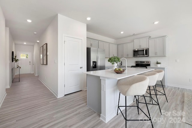 kitchen with gray cabinets, light hardwood / wood-style floors, a breakfast bar area, stainless steel appliances, and a center island with sink