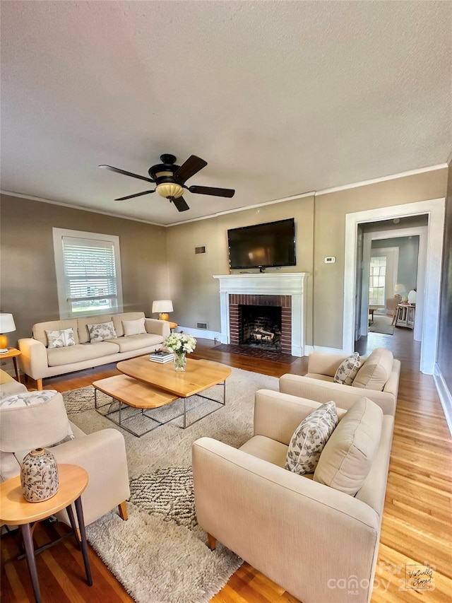 living room featuring ceiling fan, a brick fireplace, hardwood / wood-style floors, and a textured ceiling