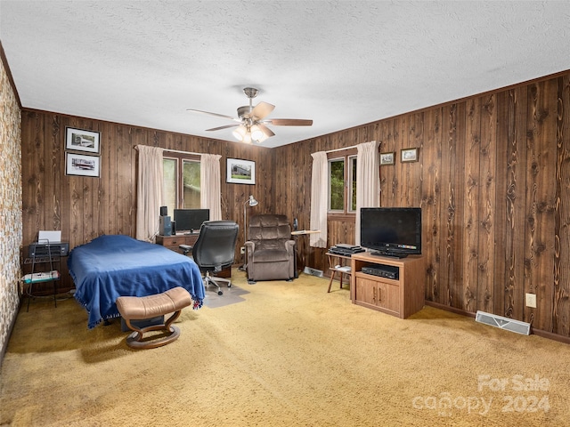 carpeted bedroom with a textured ceiling, ceiling fan, wooden walls, and multiple windows