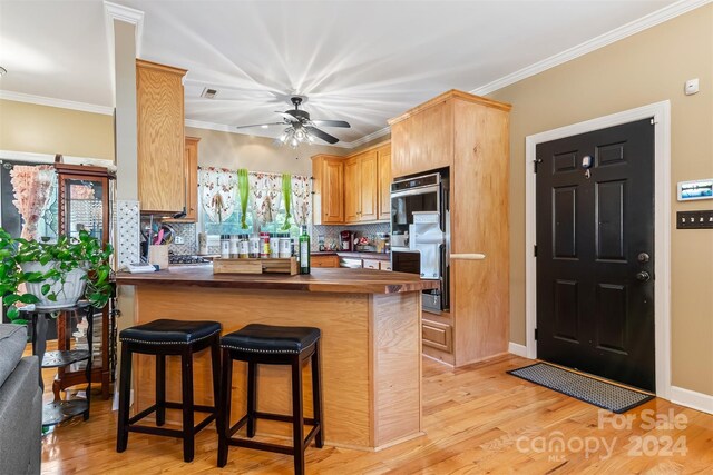 kitchen with light hardwood / wood-style flooring, kitchen peninsula, crown molding, and a kitchen bar