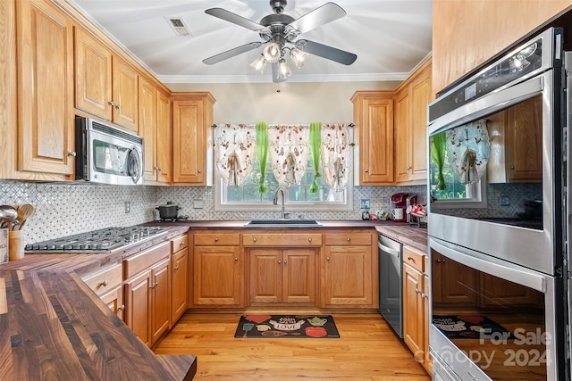 kitchen with sink, butcher block counters, ornamental molding, and stainless steel appliances