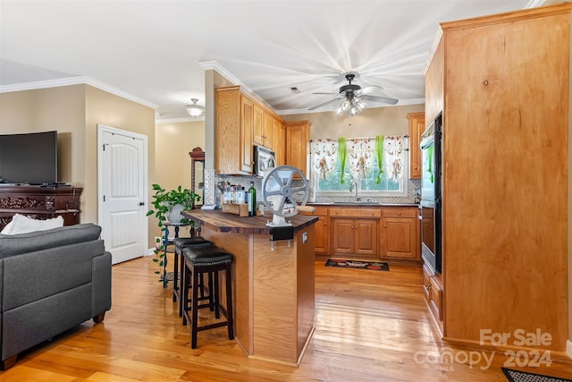 kitchen with appliances with stainless steel finishes, sink, backsplash, light wood-type flooring, and a breakfast bar area