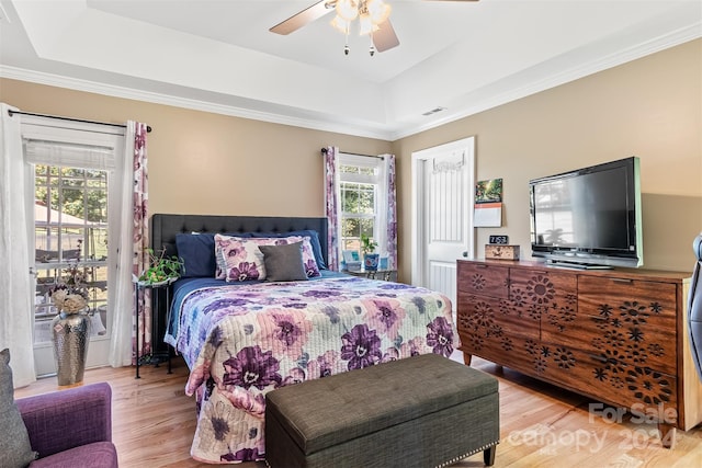 bedroom featuring ceiling fan, multiple windows, light hardwood / wood-style flooring, and a raised ceiling