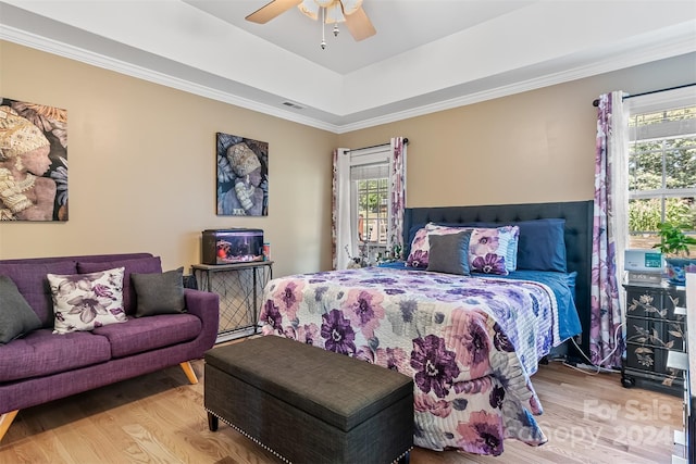 bedroom featuring ceiling fan, ornamental molding, wood-type flooring, and a tray ceiling