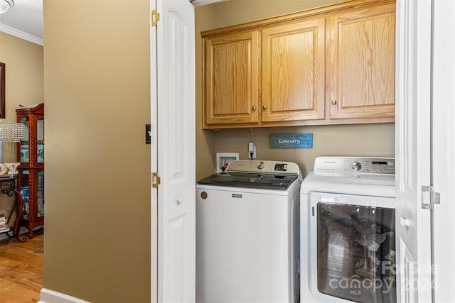 clothes washing area featuring hardwood / wood-style floors, washing machine and dryer, crown molding, and cabinets