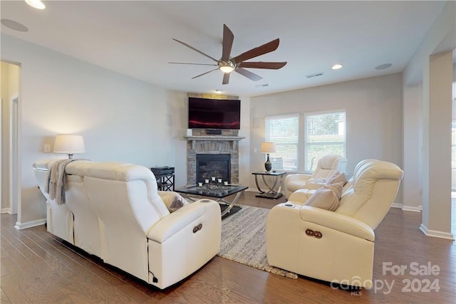 living room featuring ceiling fan, dark hardwood / wood-style floors, and a stone fireplace