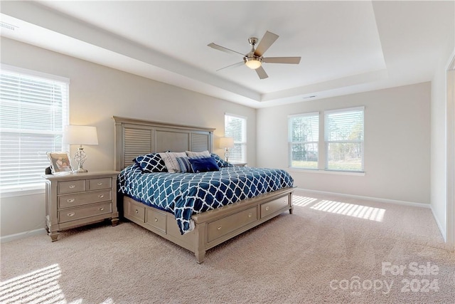 bedroom with ceiling fan, a raised ceiling, and light carpet