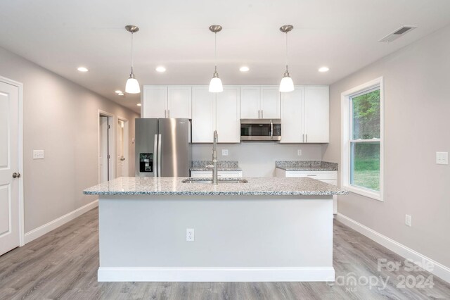 kitchen featuring light stone countertops, white cabinets, a center island with sink, and stainless steel appliances