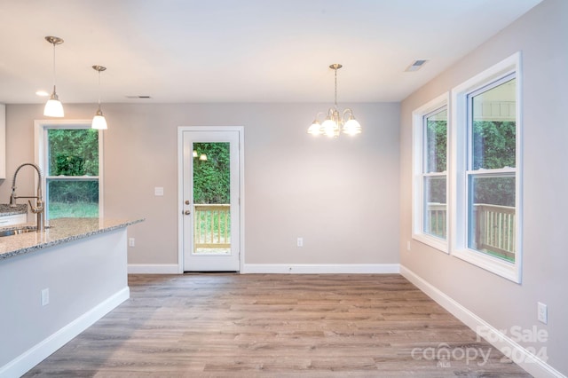 unfurnished dining area with sink, light hardwood / wood-style flooring, and a chandelier