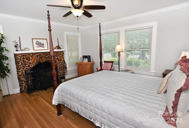 bedroom featuring ceiling fan, ornamental molding, hardwood / wood-style floors, and a stone fireplace