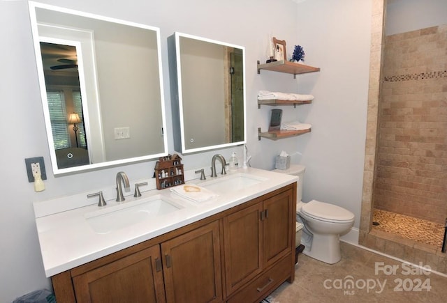 bathroom with toilet, tile patterned flooring, tiled shower, and vanity