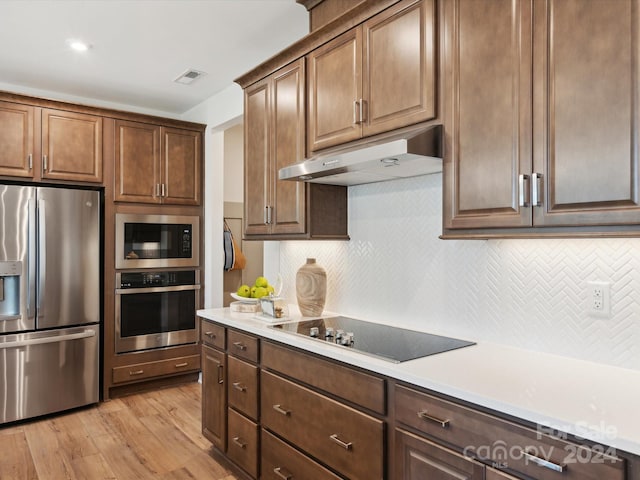 kitchen with black appliances, decorative backsplash, and light wood-type flooring