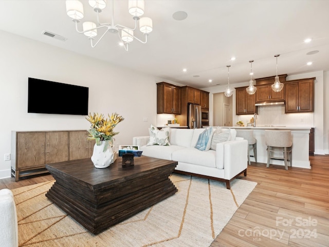 living room with sink, light hardwood / wood-style flooring, and an inviting chandelier