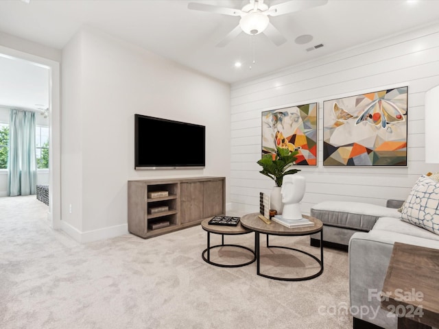 carpeted living room with ceiling fan and wood walls