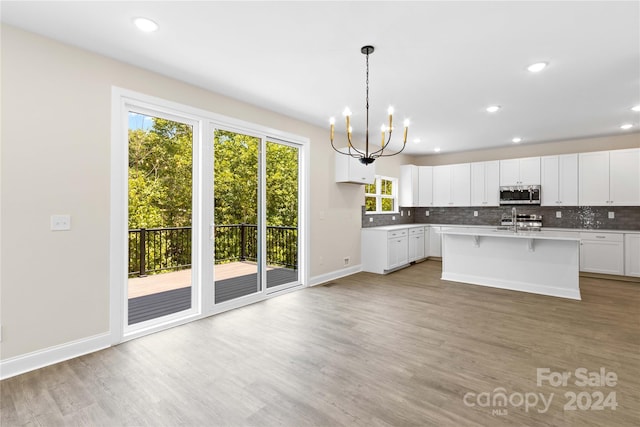 kitchen with a chandelier, white cabinets, pendant lighting, a kitchen island with sink, and backsplash