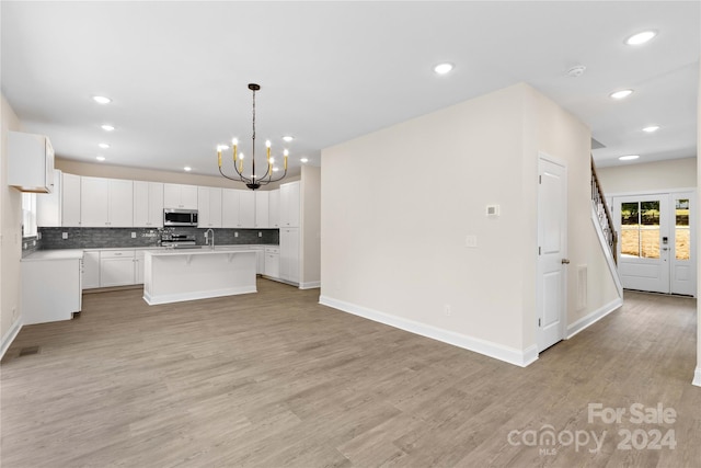 kitchen with pendant lighting, appliances with stainless steel finishes, a kitchen island with sink, white cabinetry, and tasteful backsplash