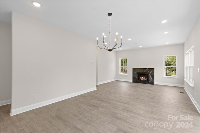 unfurnished living room with a chandelier, a high end fireplace, and light hardwood / wood-style flooring