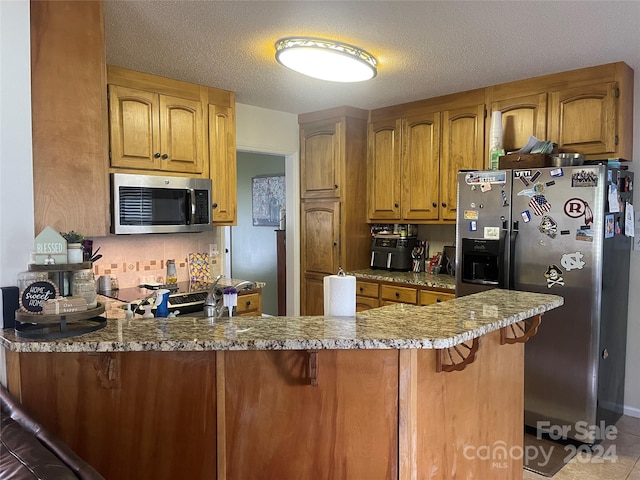 kitchen with a breakfast bar, kitchen peninsula, appliances with stainless steel finishes, and a textured ceiling