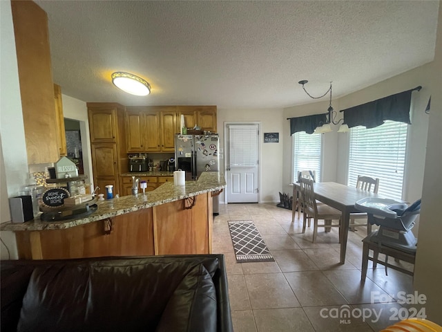 kitchen featuring kitchen peninsula, stainless steel refrigerator with ice dispenser, light tile patterned flooring, hanging light fixtures, and a chandelier