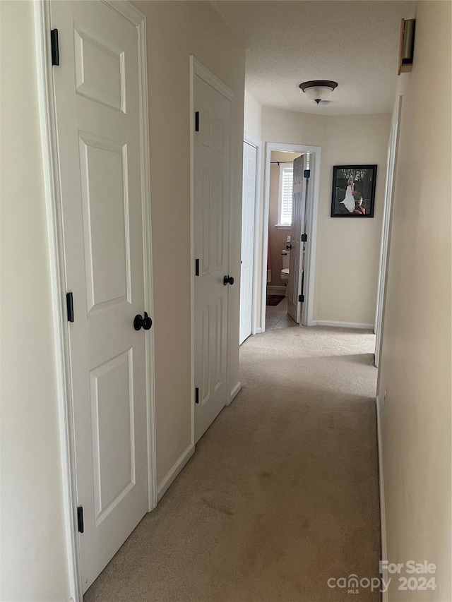 hallway featuring light colored carpet and a textured ceiling