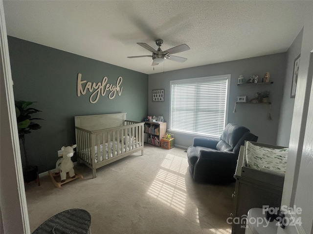 carpeted bedroom featuring a textured ceiling, ceiling fan, and a crib