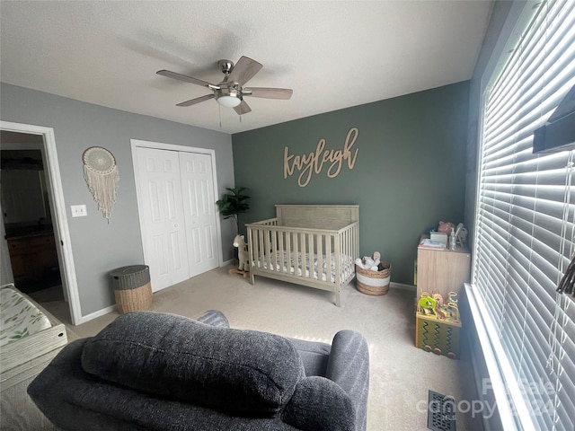 carpeted bedroom featuring ceiling fan, a closet, and a crib