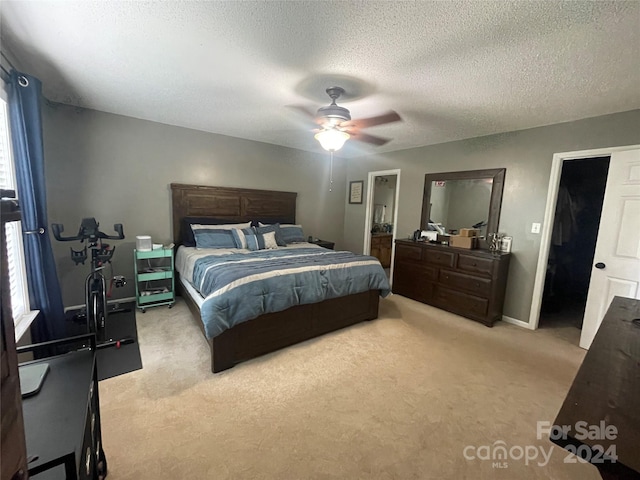 carpeted bedroom with ceiling fan, a textured ceiling, a closet, and a walk in closet