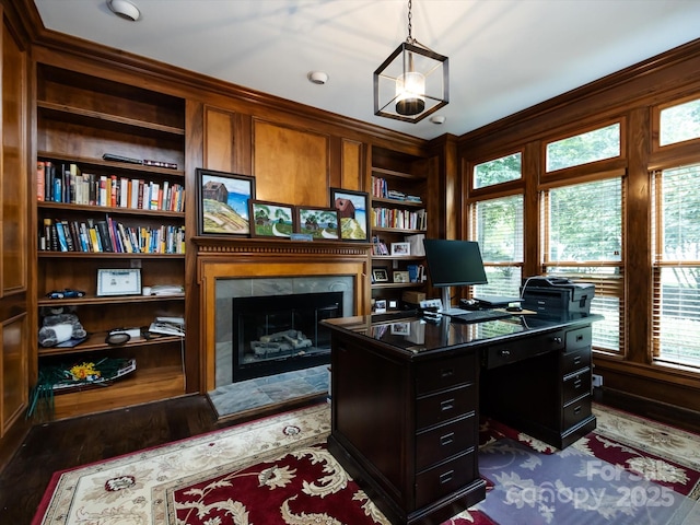 office area with dark hardwood / wood-style flooring, built in shelves, and a premium fireplace