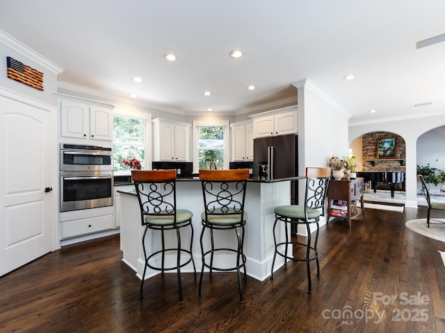 kitchen featuring a stone fireplace, stainless steel appliances, a breakfast bar, and white cabinets