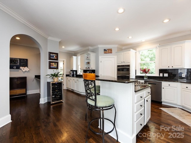 kitchen featuring white cabinetry, appliances with stainless steel finishes, a kitchen island, beverage cooler, and decorative backsplash