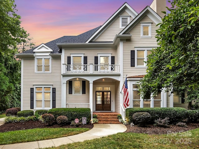 view of front of house with a porch, french doors, a balcony, and roof with shingles