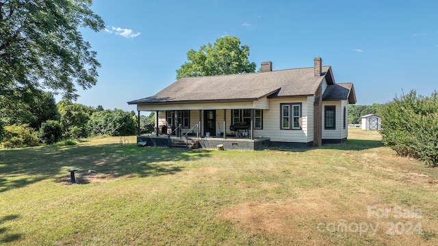 rear view of property featuring a porch, a yard, and a storage unit