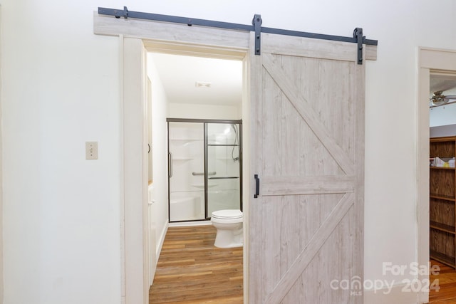 bathroom with hardwood / wood-style floors, toilet, and a shower with door