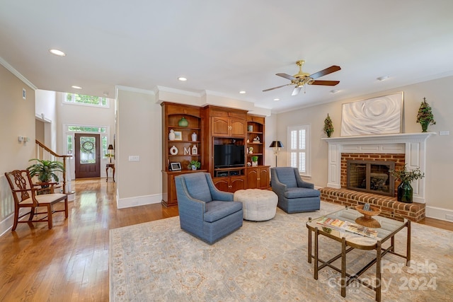 living room with light wood-type flooring, a brick fireplace, ceiling fan, and ornamental molding