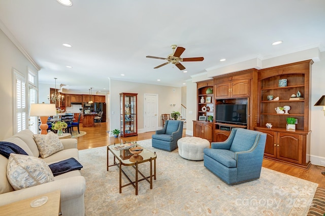 living room featuring light wood-type flooring, ceiling fan with notable chandelier, and crown molding