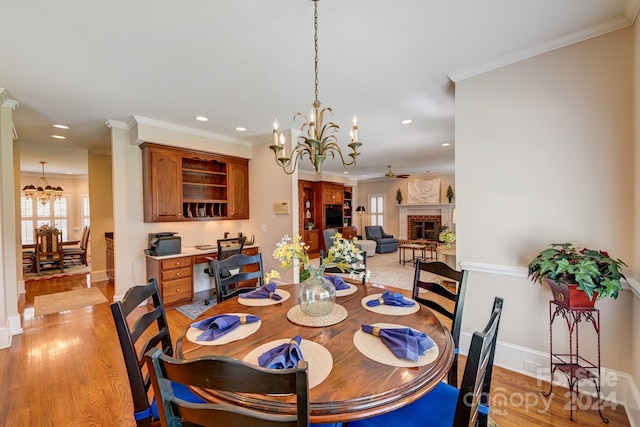 dining space with ceiling fan with notable chandelier, light wood-type flooring, a fireplace, and ornamental molding