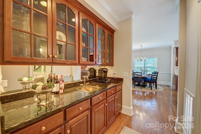 bar with dark stone counters, sink, crown molding, light wood-type flooring, and decorative light fixtures