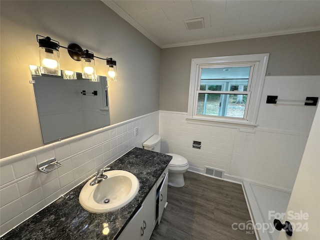 bathroom featuring tile walls, hardwood / wood-style flooring, ornamental molding, vanity, and toilet