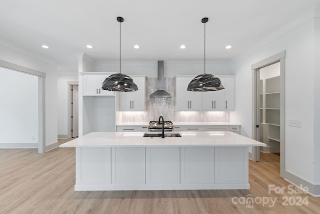 kitchen with light wood-style floors, a sink, light countertops, wall chimney range hood, and backsplash